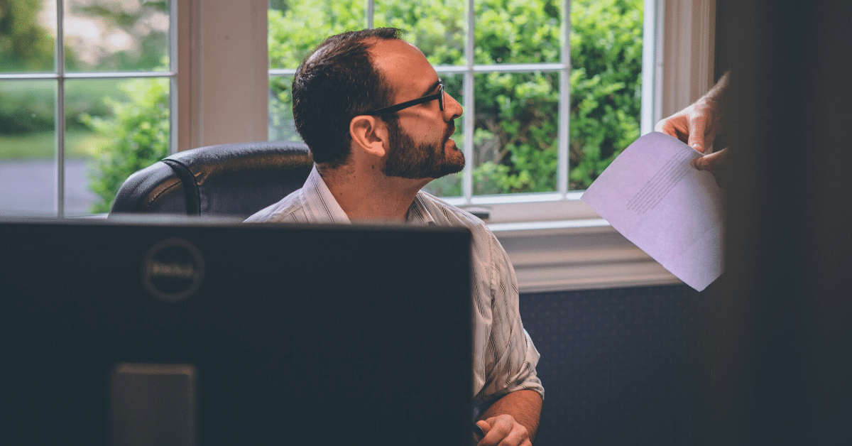 Selling Your Business to Employees - Chortek LLP - Image of a man in an office being handed a piece of paper